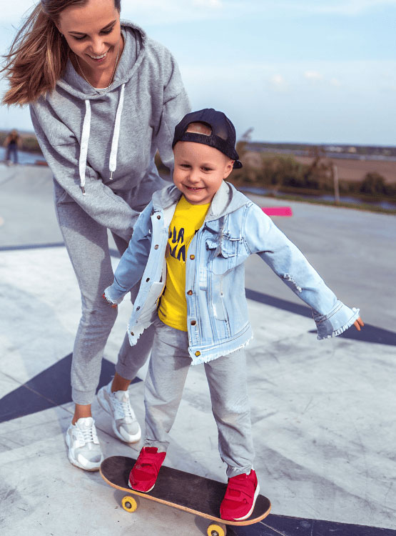 Playful mom teaching her young son to skateboard.