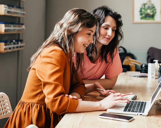 Woman holding paper and pens while looking at their laptop