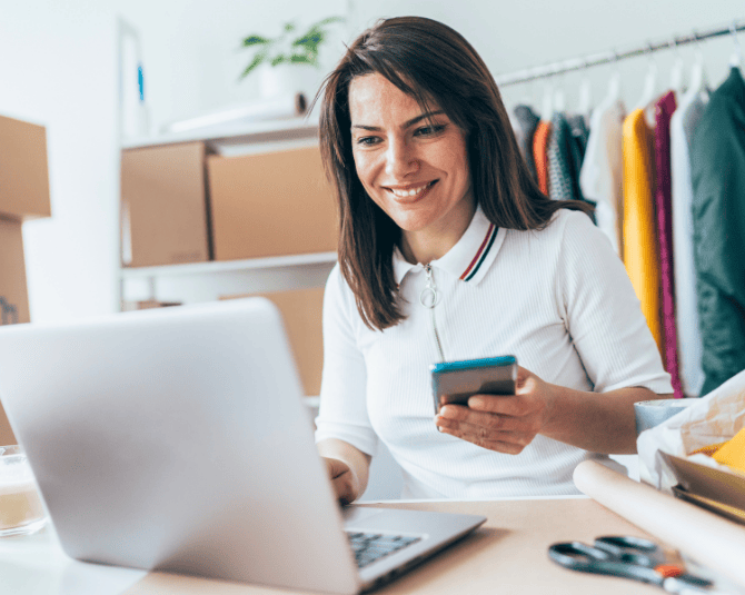 Woman holding her phone while looking at her laptop