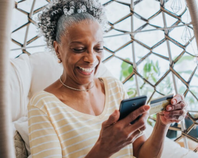 Woman looking at her debit card and her phone while smiling