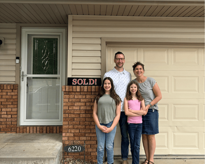 Family posing in font of their new home with a sold sign