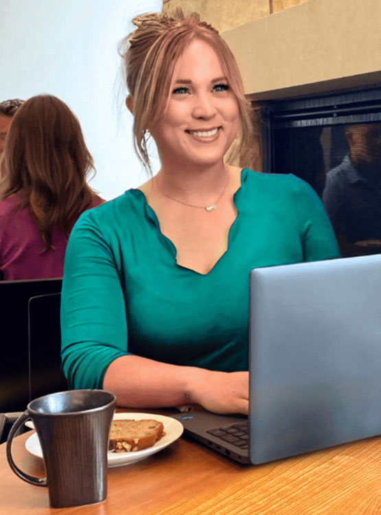 Smiling young girl looking a her computer screen sitting at a table.