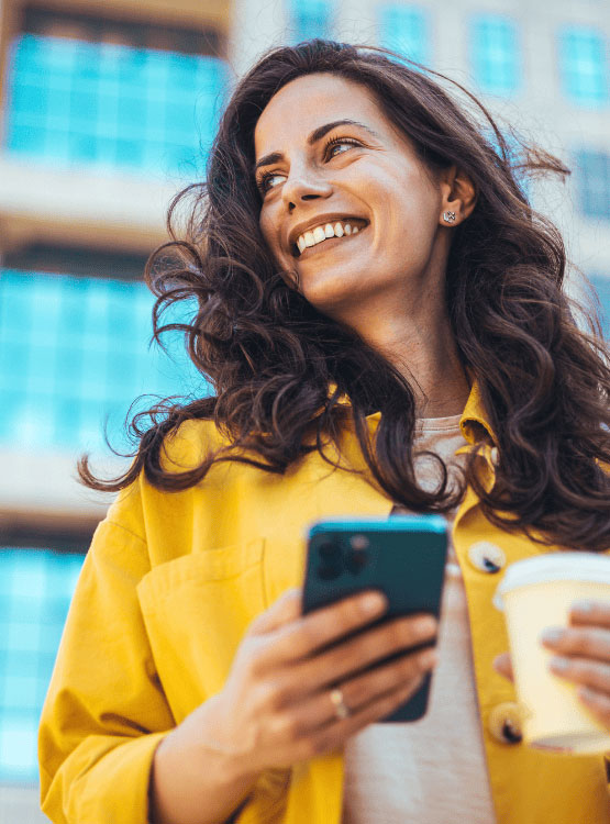 Smiling young woman drinking coffee and using her smartphone.