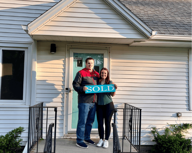 Couple holding a SOLD sign in front of their new house